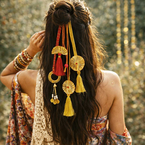 Woman with long hair adorned with decorative hair accessories and bangles, standing against a blurred natural background. Suwasna Pink & Gold Boho Tassel Hair Tie with Fan Charms & Bead Detailing | Stylish Festival, Beach & Casual Hair Accessory Design-5